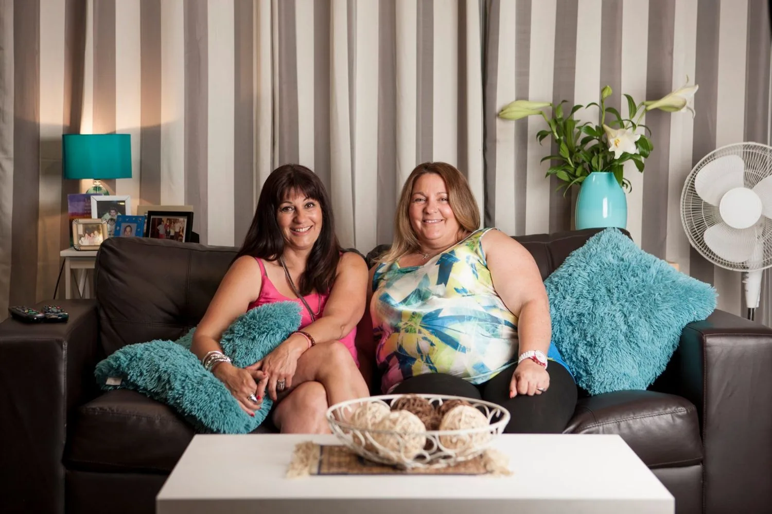Faye and Anastasia together on a leather couch with fluffy blue cushions