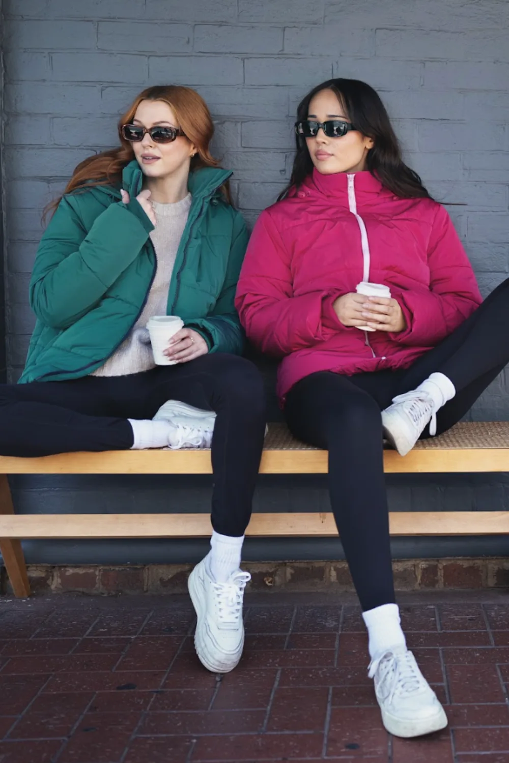 two women sitting on a bench one wearing the oodie greenjacket and another wearing the oodie pink jacket 