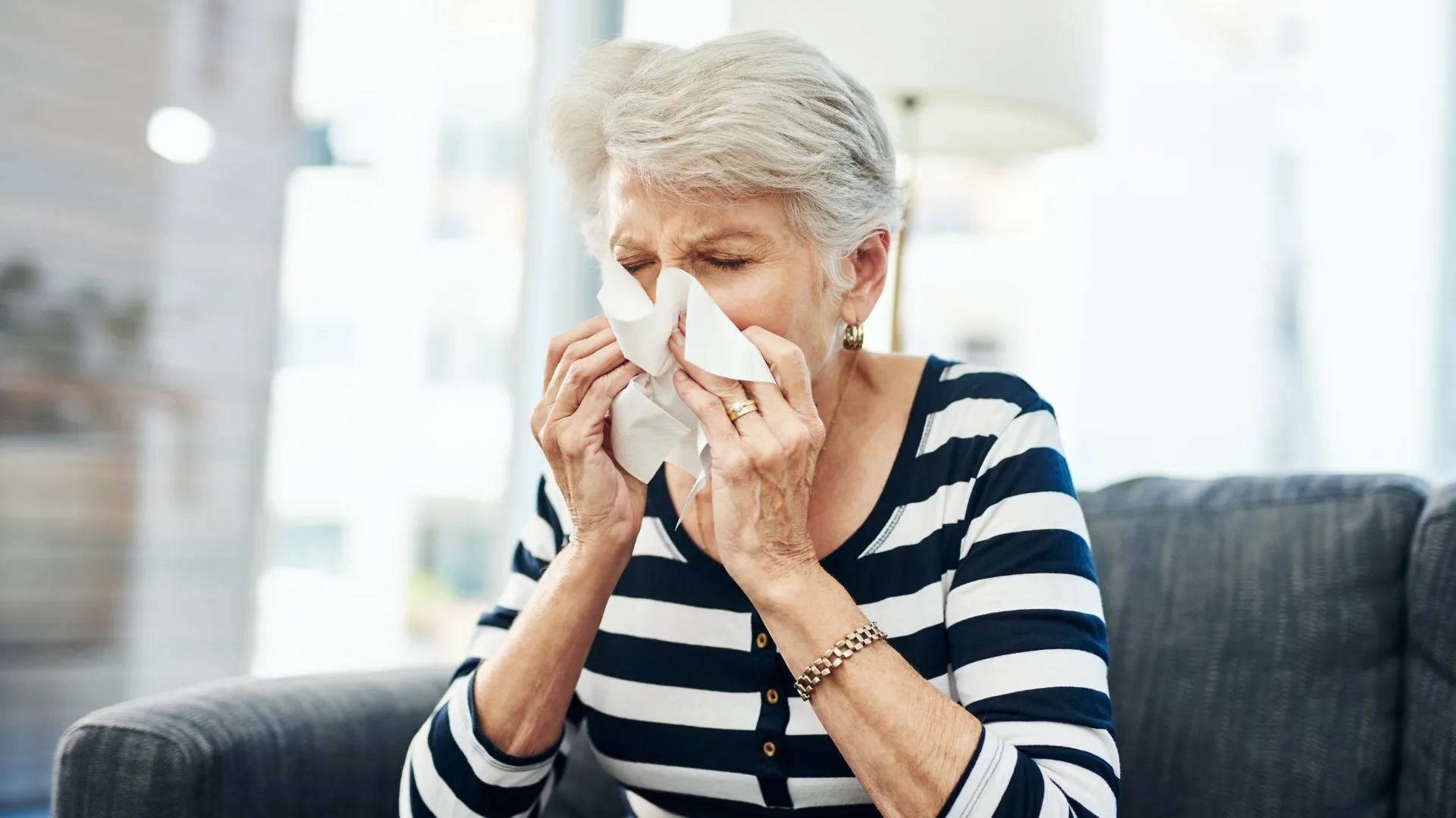 older woman sneezing into tissue