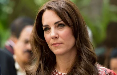 A woman with long brown hair and a patterned top looks thoughtful outdoors.