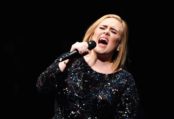 Singing performer in a sparkly dress holding a microphone on stage, eyes closed, expressing emotion.