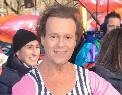Man in a colorful outfit at an outdoor event with people and balloons in the background.