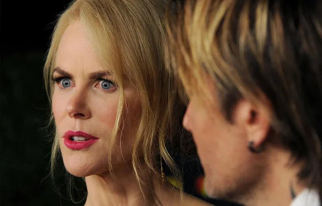 A surprised woman with blonde hair talking to a man with highlighted hair, partially visible from behind.