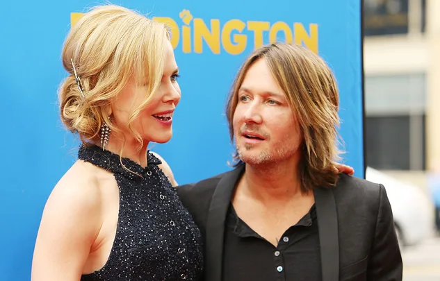 A man and woman smile at each other on a red carpet with a blue background, attending a public event.