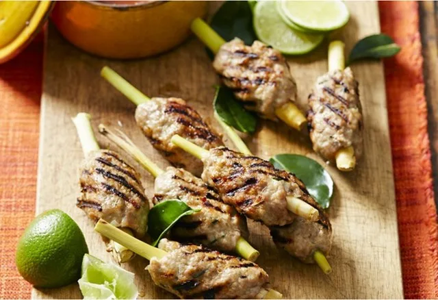 Grilled Vietnamese lemongrass pork skewers on a wooden board with lime and herbs.