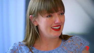 A woman with long hair is visibly emotional, wearing a blue lace top and red lipstick.