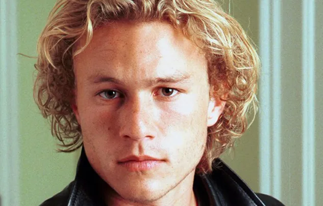 Young man with curly blonde hair in a leather jacket, looking serious.
