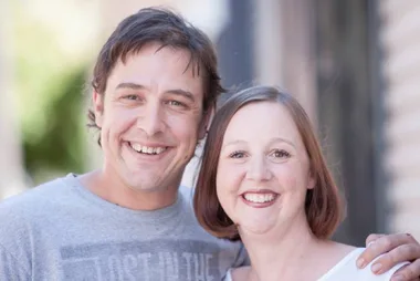 Two smiling people embracing outdoors.