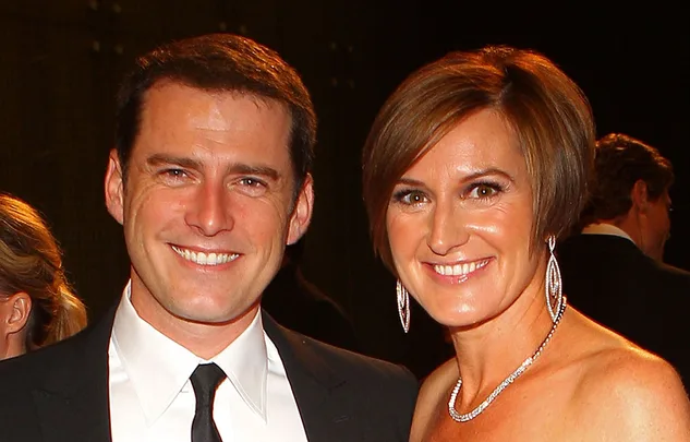 A man and woman smiling at a formal event, the man in a suit and the woman in a dress with earrings.