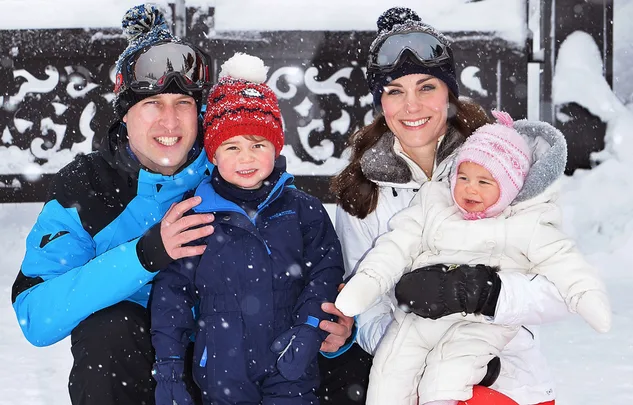 Family bundled up in winter gear poses outside in snowy setting.