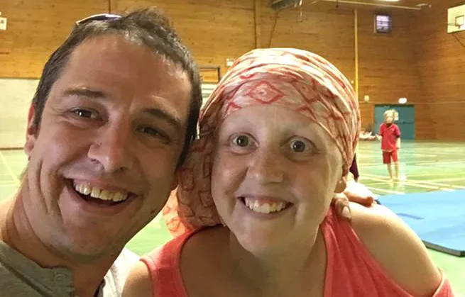 Two people smiling in a gymnasium; one wearing a headscarf.