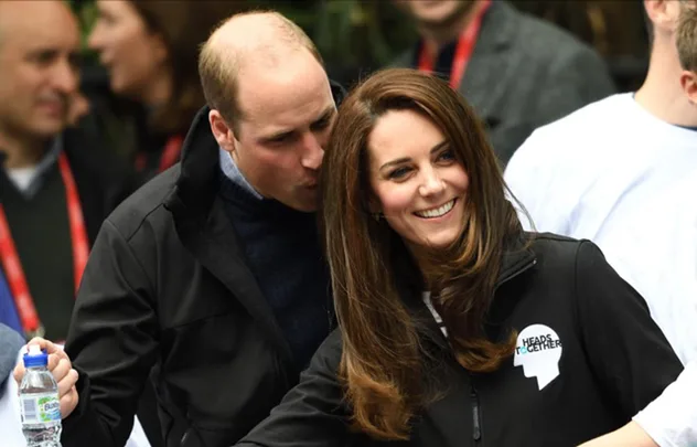 Prince William leans in affectionately toward Duchess Catherine at a public event, smiling in an outdoor setting.