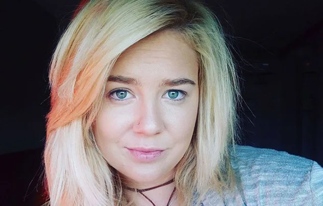A woman with long blonde hair and a nose piercing, looking directly at the camera.