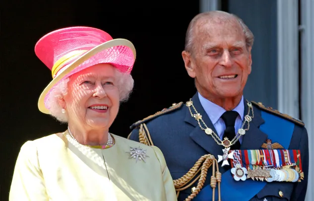 Two elderly people smiling, one in a pink hat and yellow outfit, the other in a military uniform with medals.
