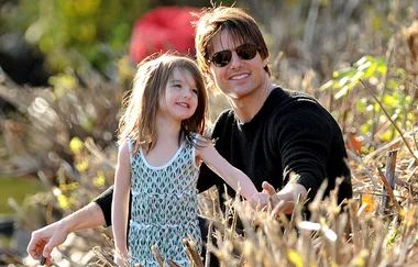 Father and young daughter smiling while sitting outdoors among bushes on a sunny day.