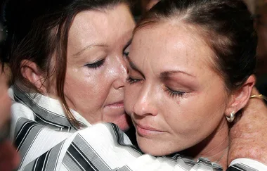 A woman with teary eyes is hugging another woman closely, both appearing emotional.