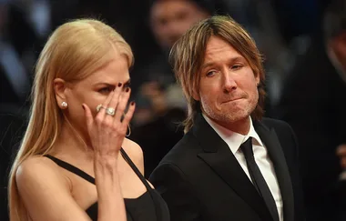 Female in black dress and male in suit on red carpet, woman's hand near face, emotional atmosphere.