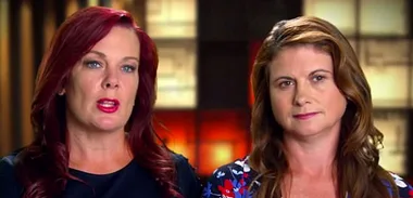 Two women with serious expressions, one with red hair and the other with brown hair, in a speaking scene.