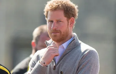 I don't know who this person is. A person with red hair and a beard, wearing a gray sweater, stands outdoors looking thoughtful.