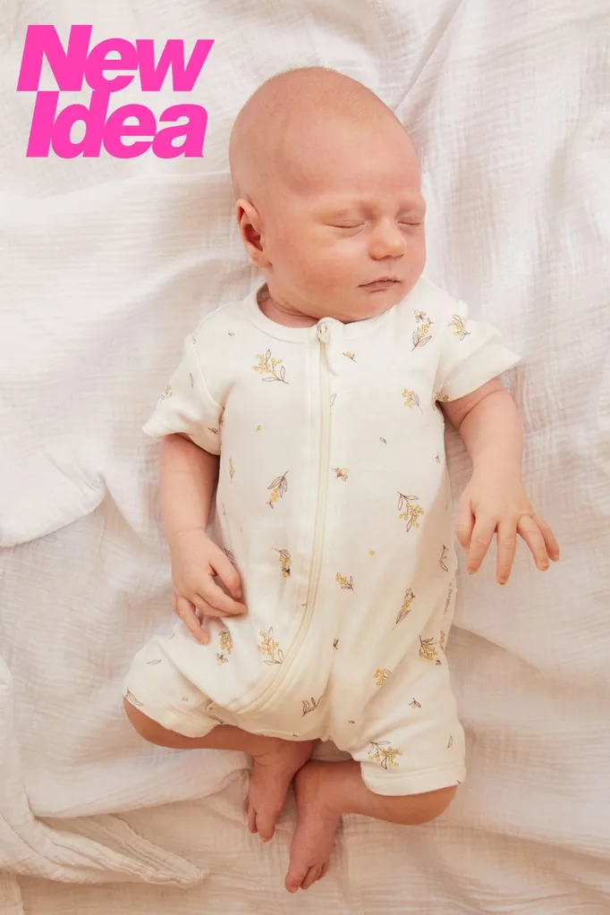 Baby in white jumpsuit lying on bed