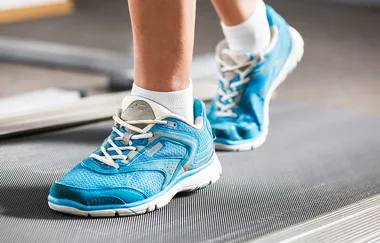 Feet in blue sneakers walking on a treadmill, emphasizing fitness and exercise.