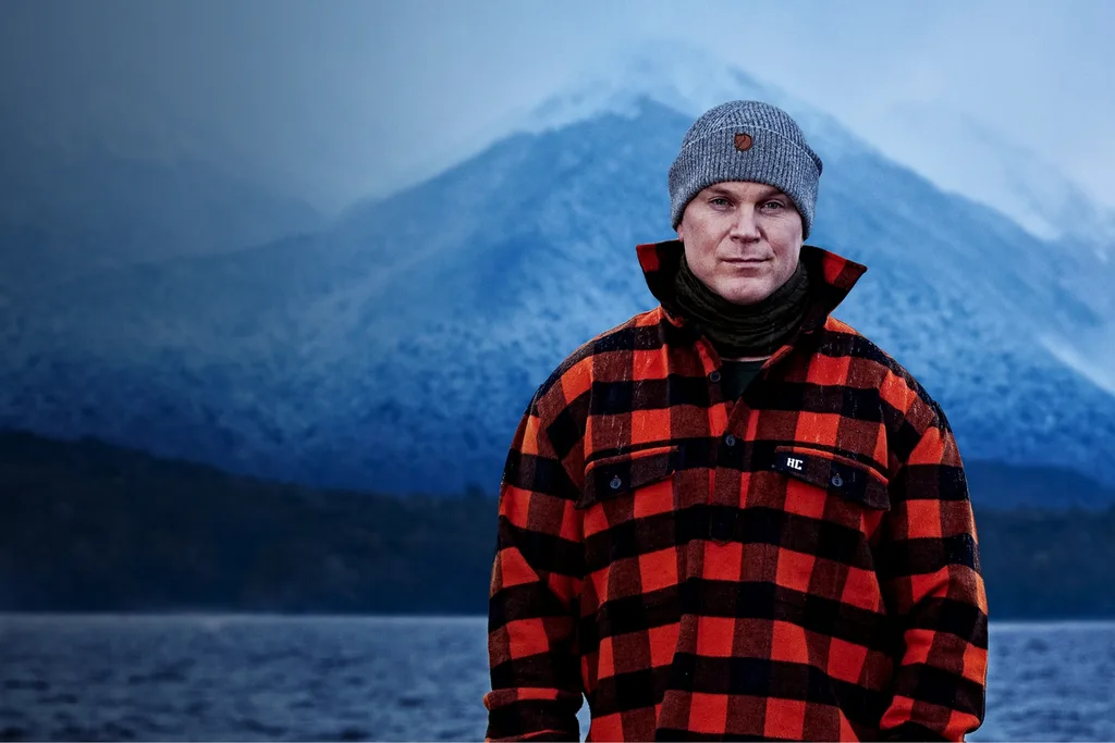 Alone contestant Andreas standing outdoors wearing a red and black coat in a cold environment.