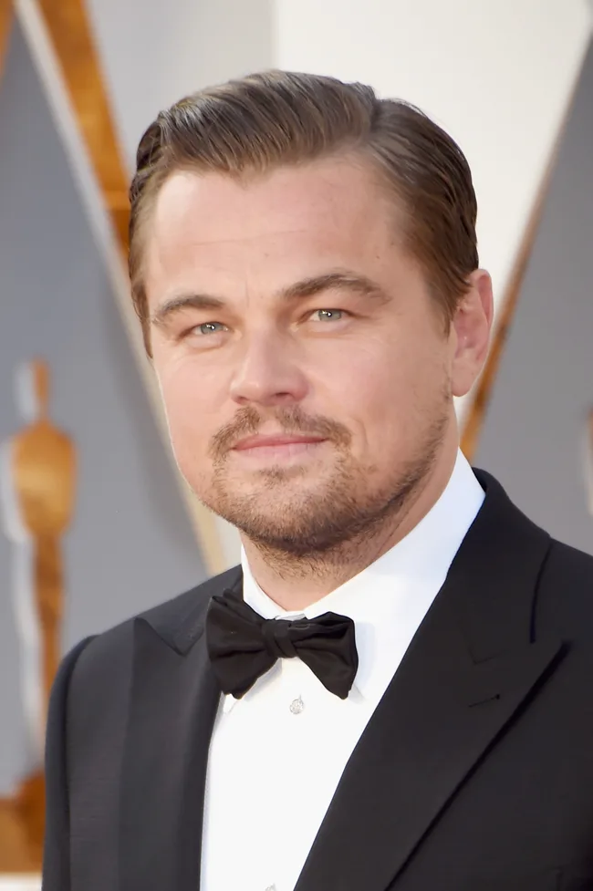 A man in a tuxedo with a bow tie, at a formal event with a blurred background.