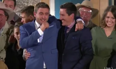 Group celebrating, two men in suits with arms around each other, one in blue, smiling among a cheering crowd.