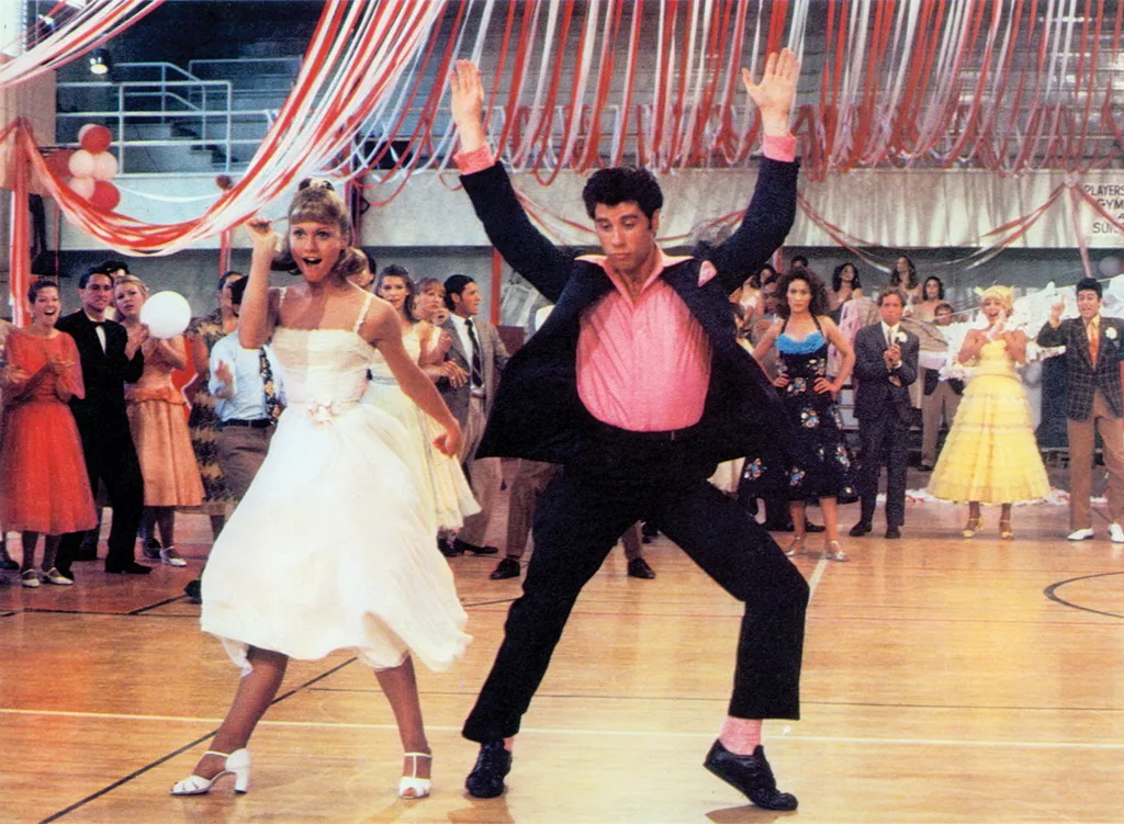 A couple dances enthusiastically in a gym decorated with red ribbons, surrounded by a cheering crowd.