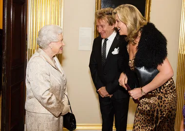 Three people in formal attire smiling and conversing indoors.