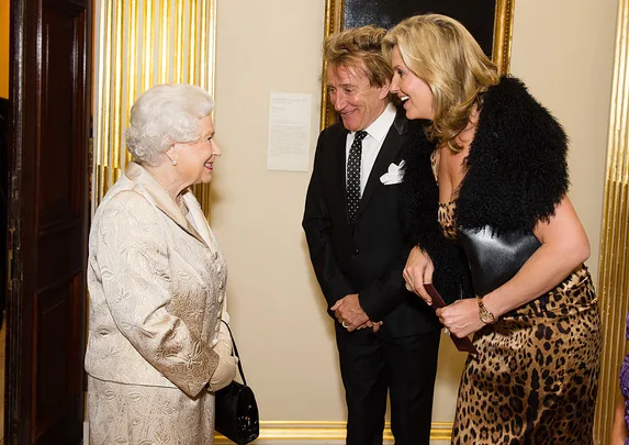 Three people in formal attire smiling and conversing indoors.