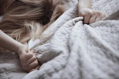 Woman clutching bedding while having sex