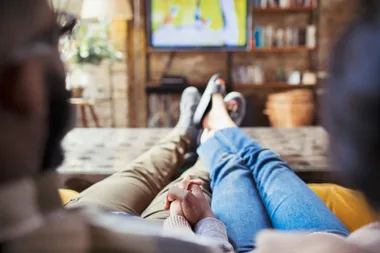 Couple holding hands on couch watching TV