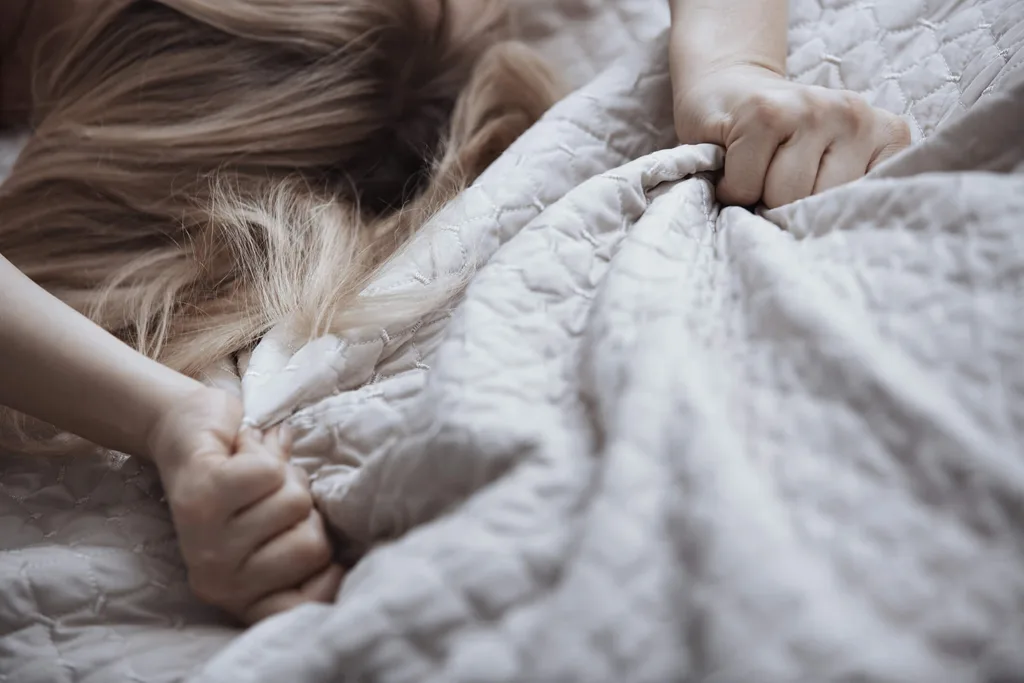 Woman clutching bed sheets during orgasm