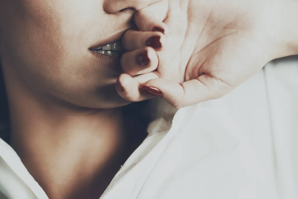A girl holding hand in front of face while smiling seductively