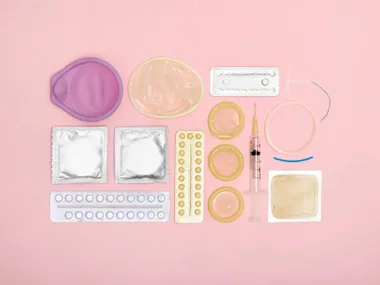 Various birth control methods lying on a pink background