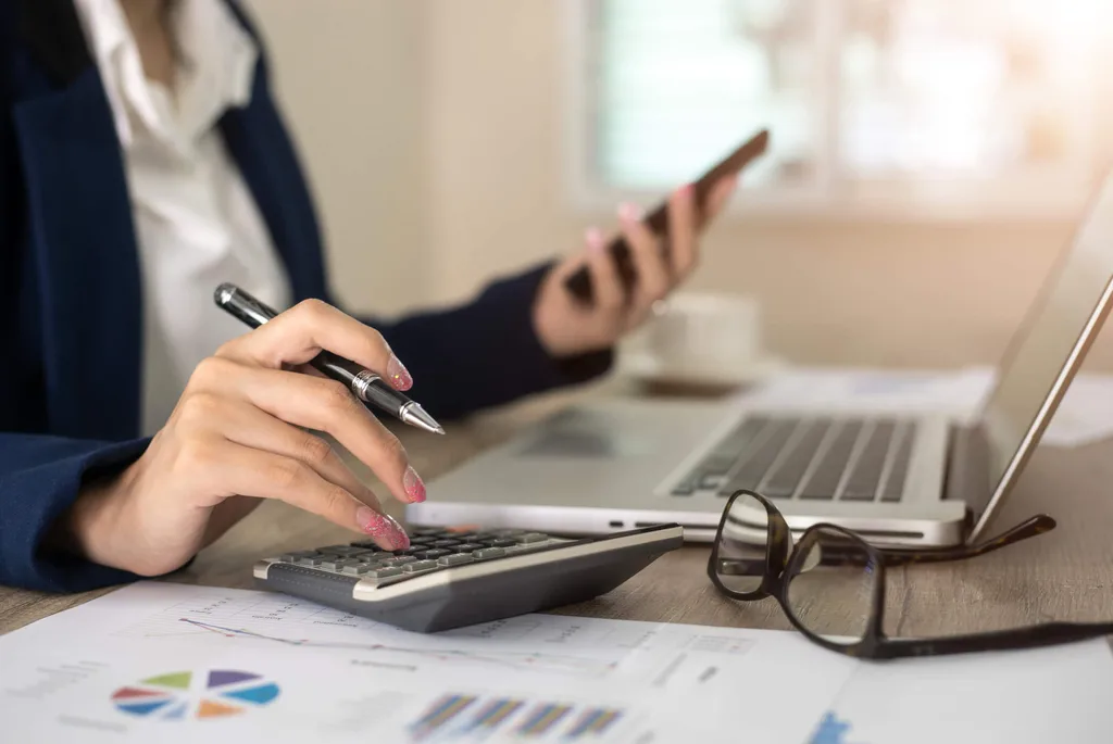 Woman using calculator while looking at laptop