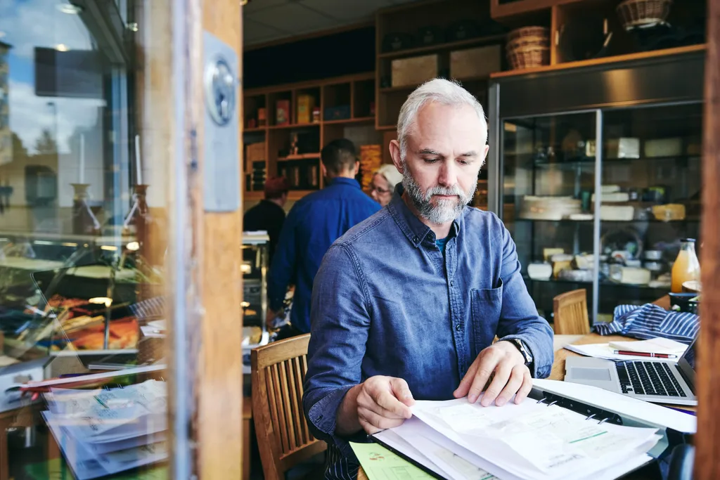 Old man in blue buttonup shirt reading papers in a cafe