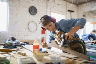 Female carpenter sanding a piece of wood