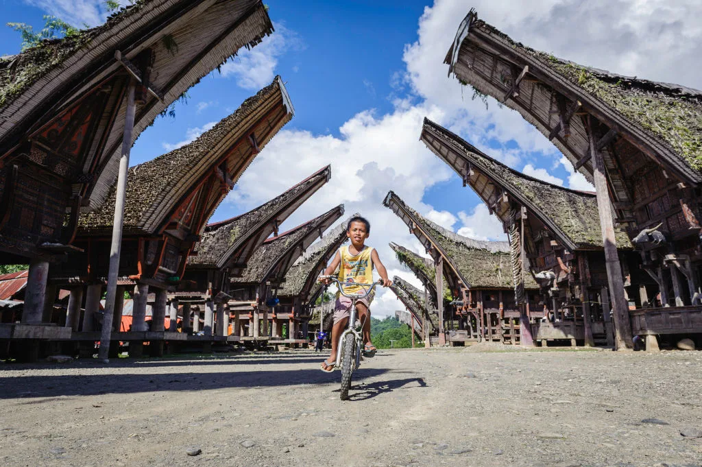 Young boy riding a bike through rows of houses in a Tana Toraja village