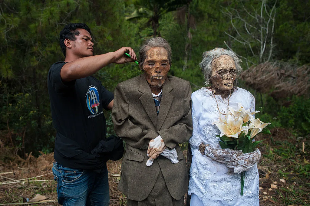 An Indonesian man combing the hair of his dead grandparents during a ma-nene ritual.