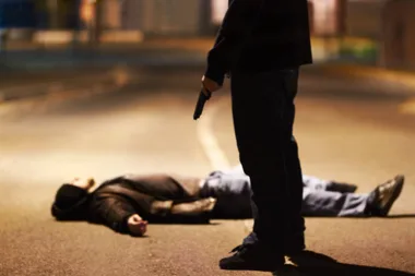 A man lying on a road with a armed criminal on top