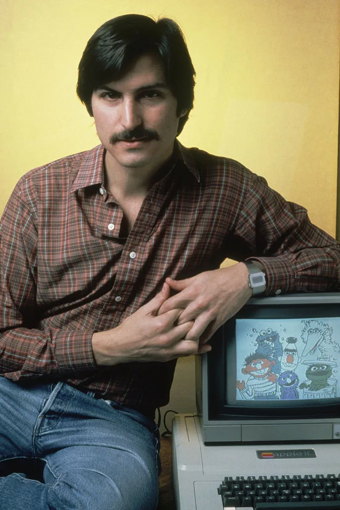 Steve Jobs leaning on the Apple II Computer