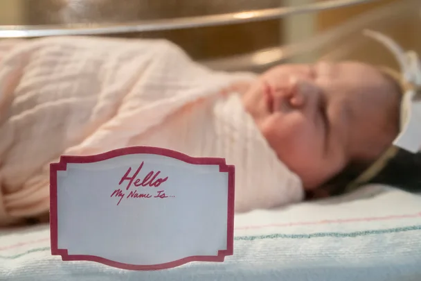 A name tag with 'Hello My Name Is...' written on it, with a baby behind