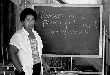 Audre Lorde in front of a blackboard with the writing 'Women are powerful and dangerous.'
