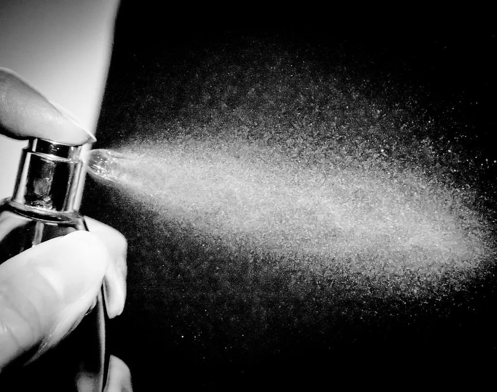 A black and white photo of a woman spraying a bottle of perfume