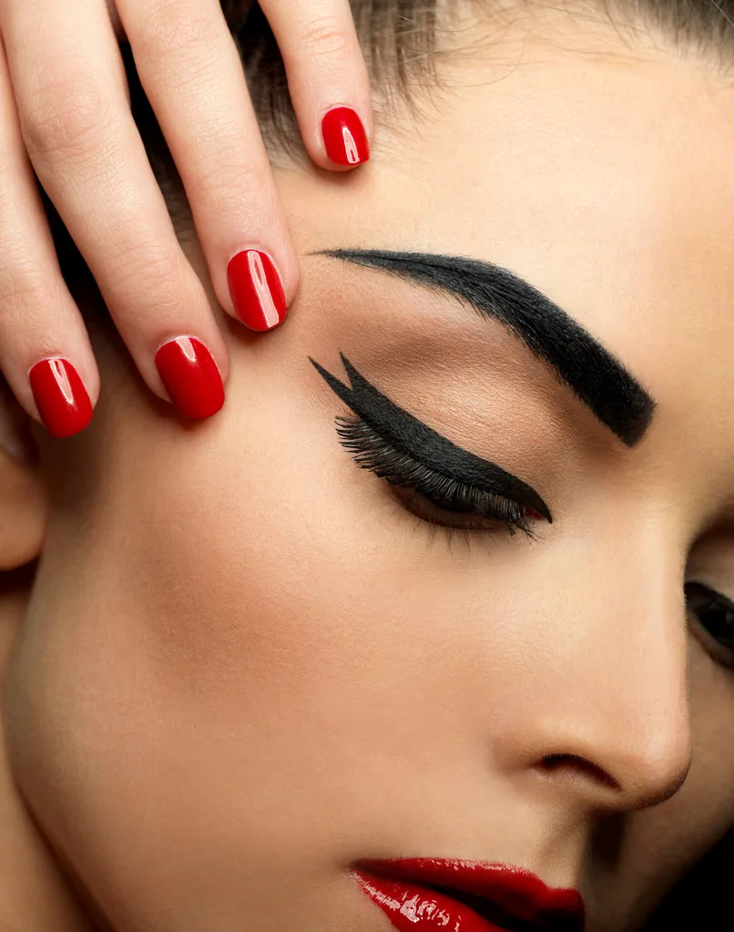 A close up of a woman's face showing her red lipstick, black eyeliner and tinted eyebrows