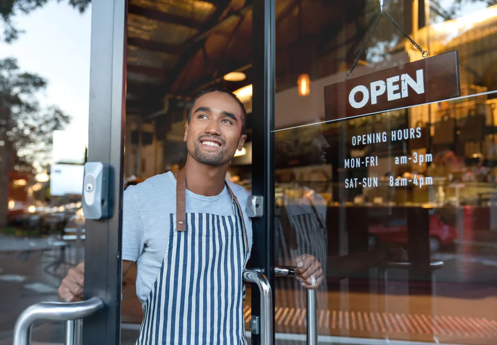 A smiling waiter opening a cafe door