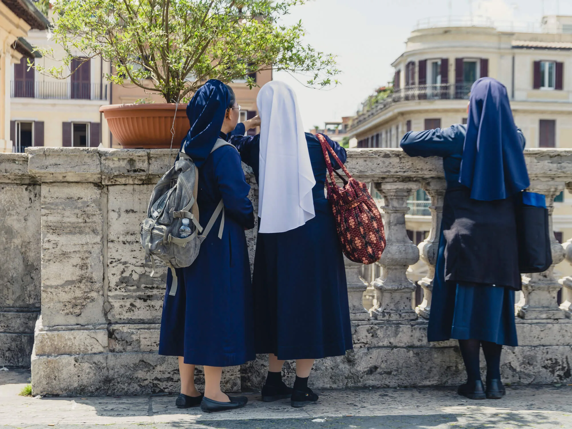 Three nuns in dresses looking over a stone wall