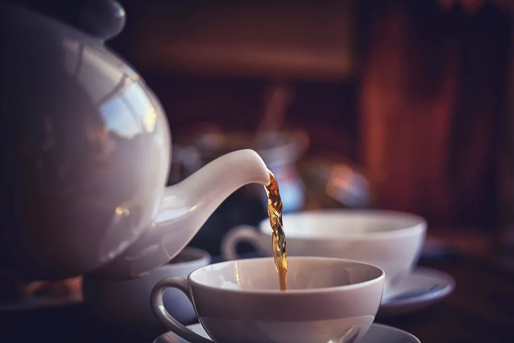 A tea pot pouring tea in a white tea cup